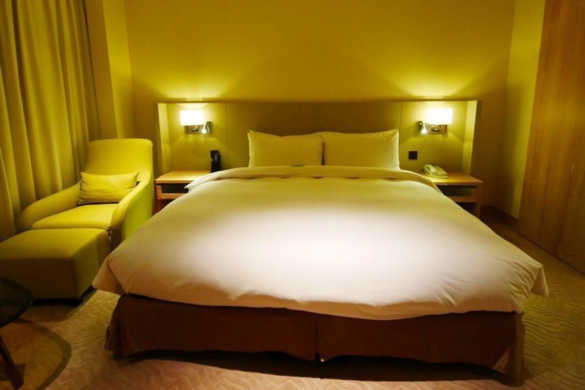 A hotel room with a large bed, two bedside lamps, a chair, and a nightstand.