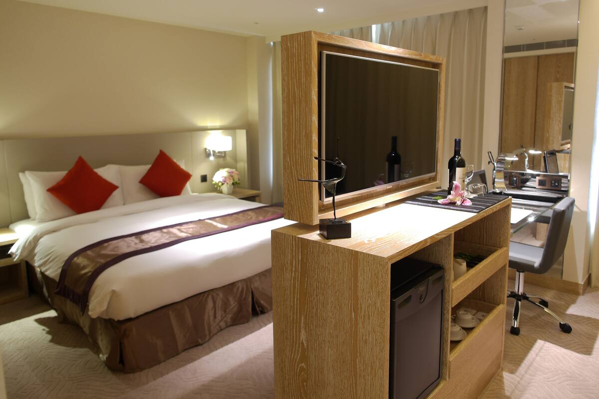 A hotel room with a bed, a desk with a mirror, a small sink, and a compact dishwasher.
