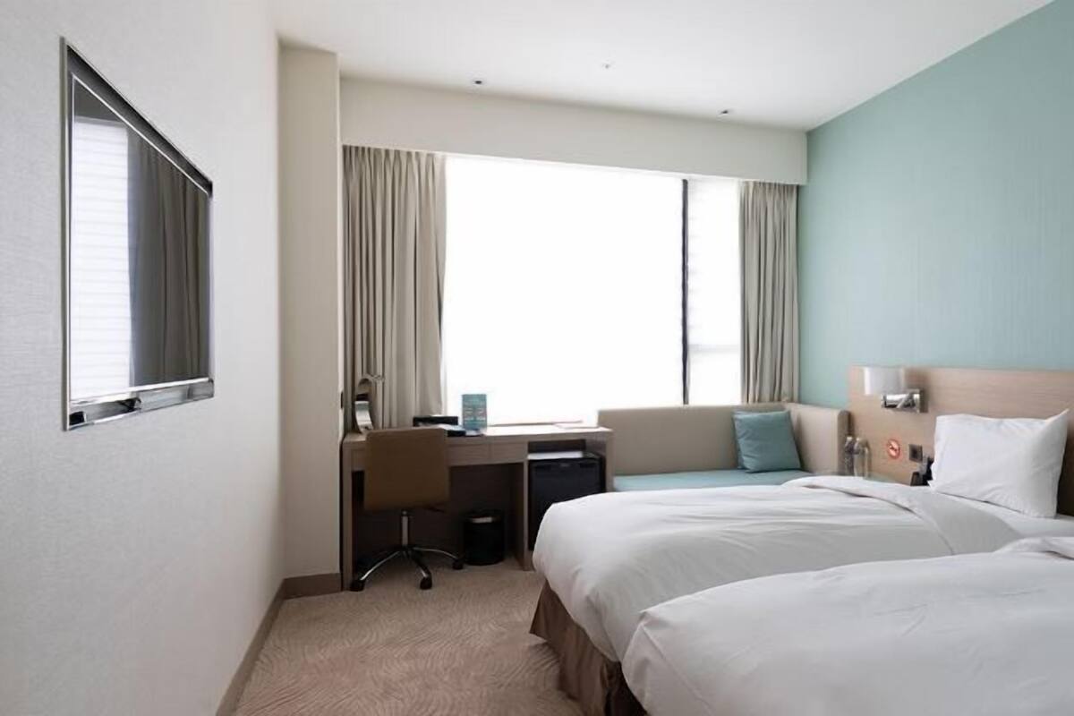 A hotel room with two beds, a desk, and a window with curtains.