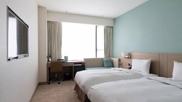 A hotel room with two beds, a desk, and a window with curtains.
