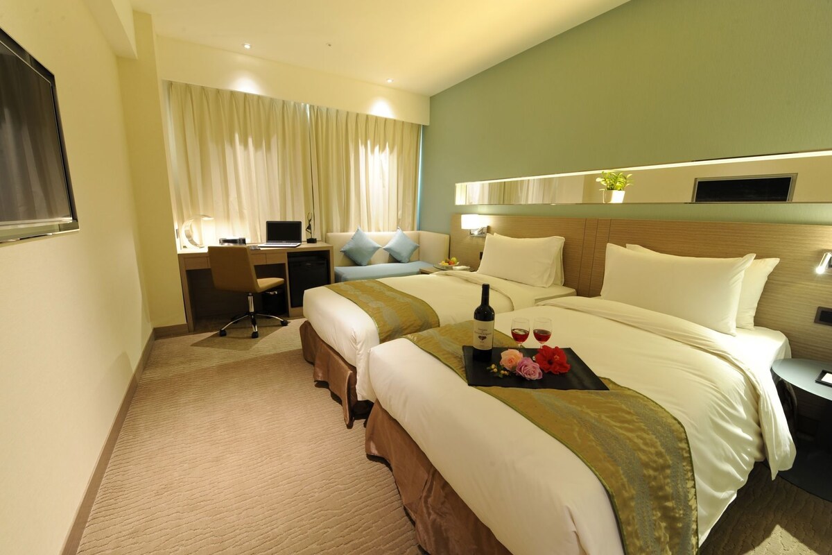 A hotel room with two beds, a desk, and a computer.