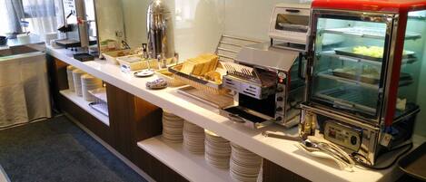 A buffet setup with a coffee machine, a toaster, and a glass display case with food items.