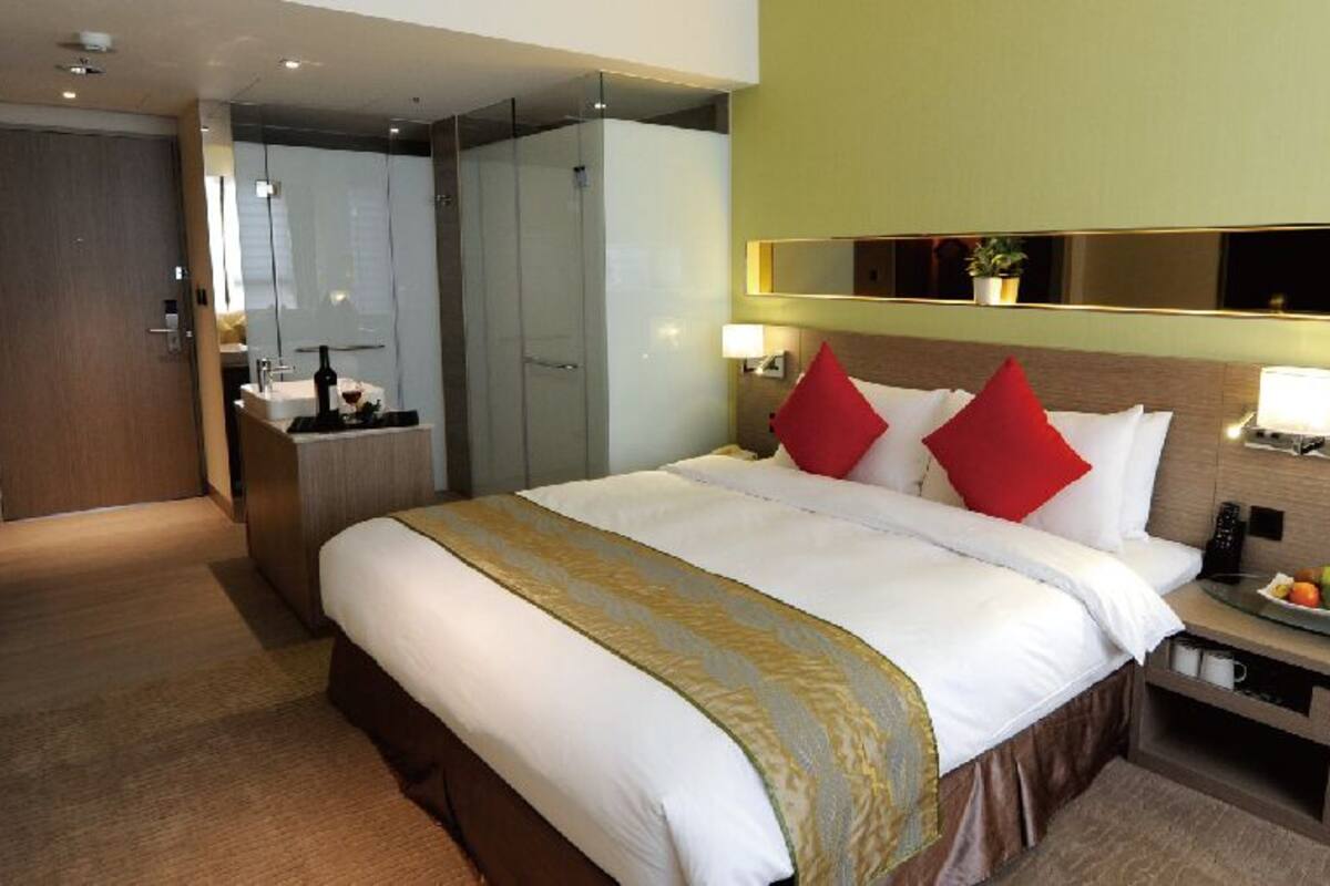 A hotel room with a large bed, bedside tables, a mirror, and a small table with fruit.