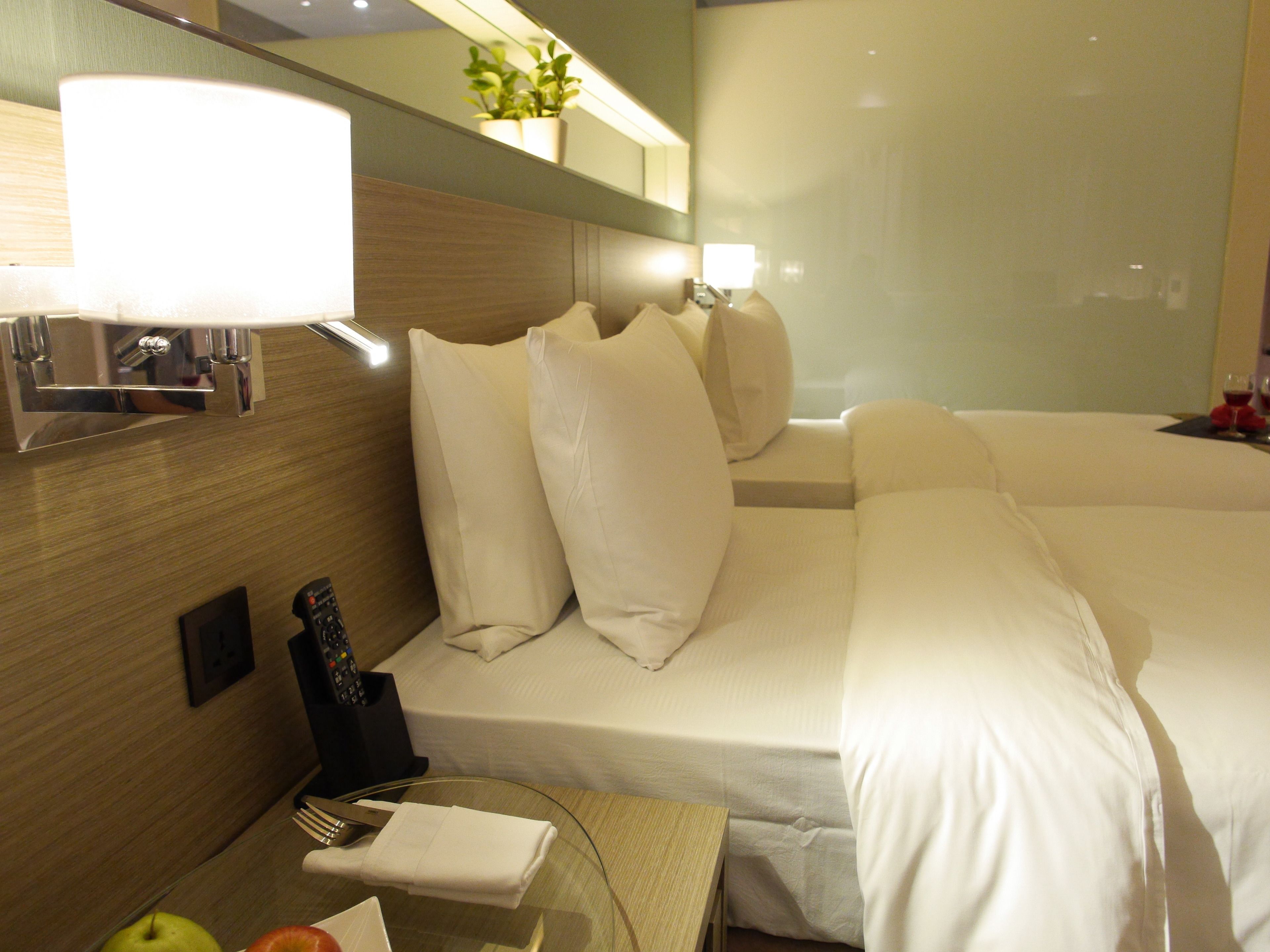 Una habitación de hotel con una cama, una mesita de noche con lámpara, un control remoto y un frutero.