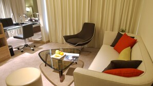 A modern living room with a glass coffee table, a white sofa with colorful cushions, a black armchair, and a round ottoman. - Kaohsiung International Plaza (Kaohsiung)