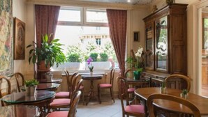 A dining area with wooden tables and chairs, a large cabinet, and potted plants. - Familia Hotel (Paris)