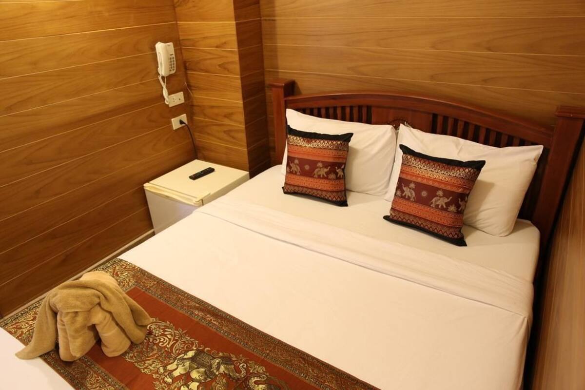 Una habitación de hotel con cabecera de madera, una mesita de noche con teléfono y dos almohadas estampadas.