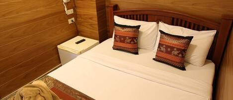 Una habitación de hotel con cabecera de madera, una mesita de noche con teléfono y dos almohadas estampadas.