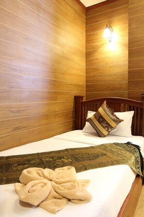 A neatly made bed with a decorative throw and a pillow, set against a wooden wall with a light fixture. - Tanee Place (Bangkok)