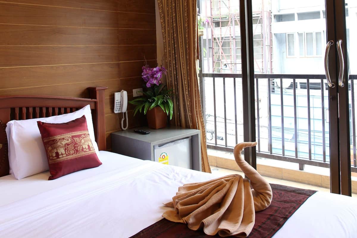 Habitación de hotel con cama, teléfono, planta en maceta y balcón con vistas a edificios.