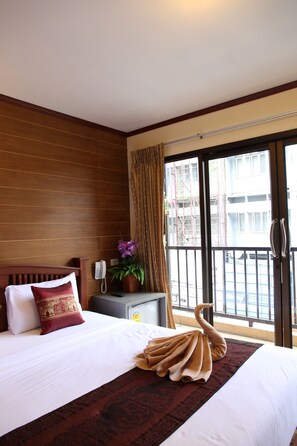 A hotel room with a bed, a telephone, a potted plant, and a balcony with a view of buildings. - Tanee Place (Bangkok)