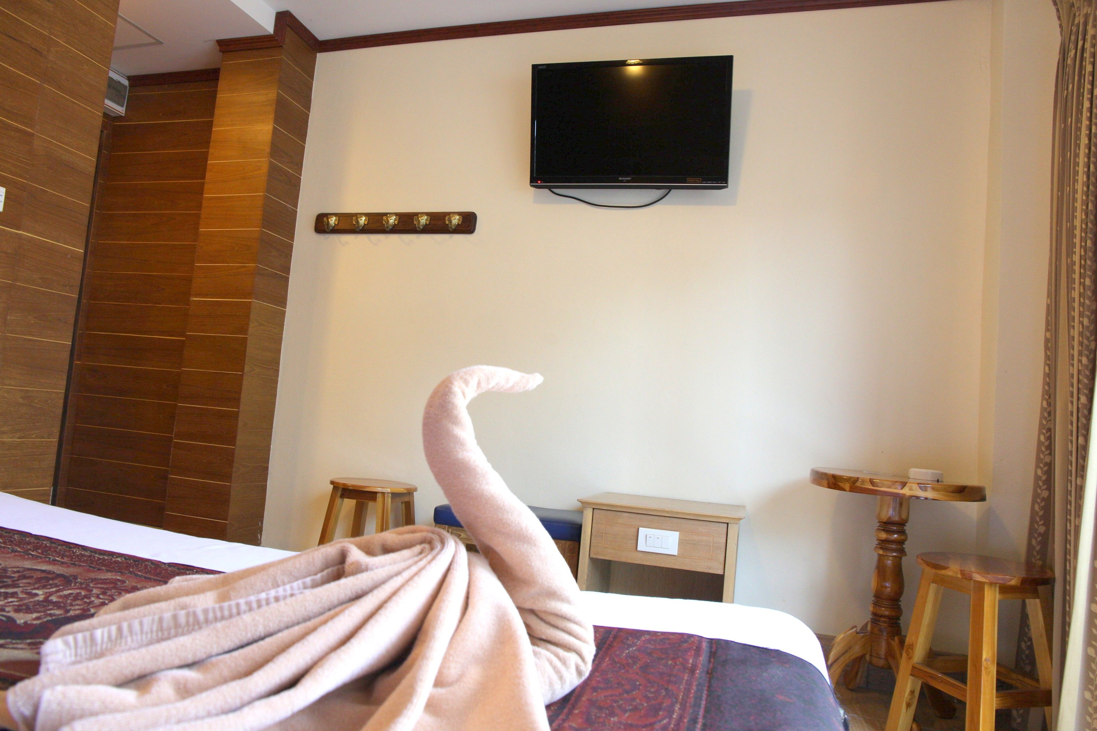 A hotel room with a bed, a television mounted on the wall, a small wooden table, and a chair.