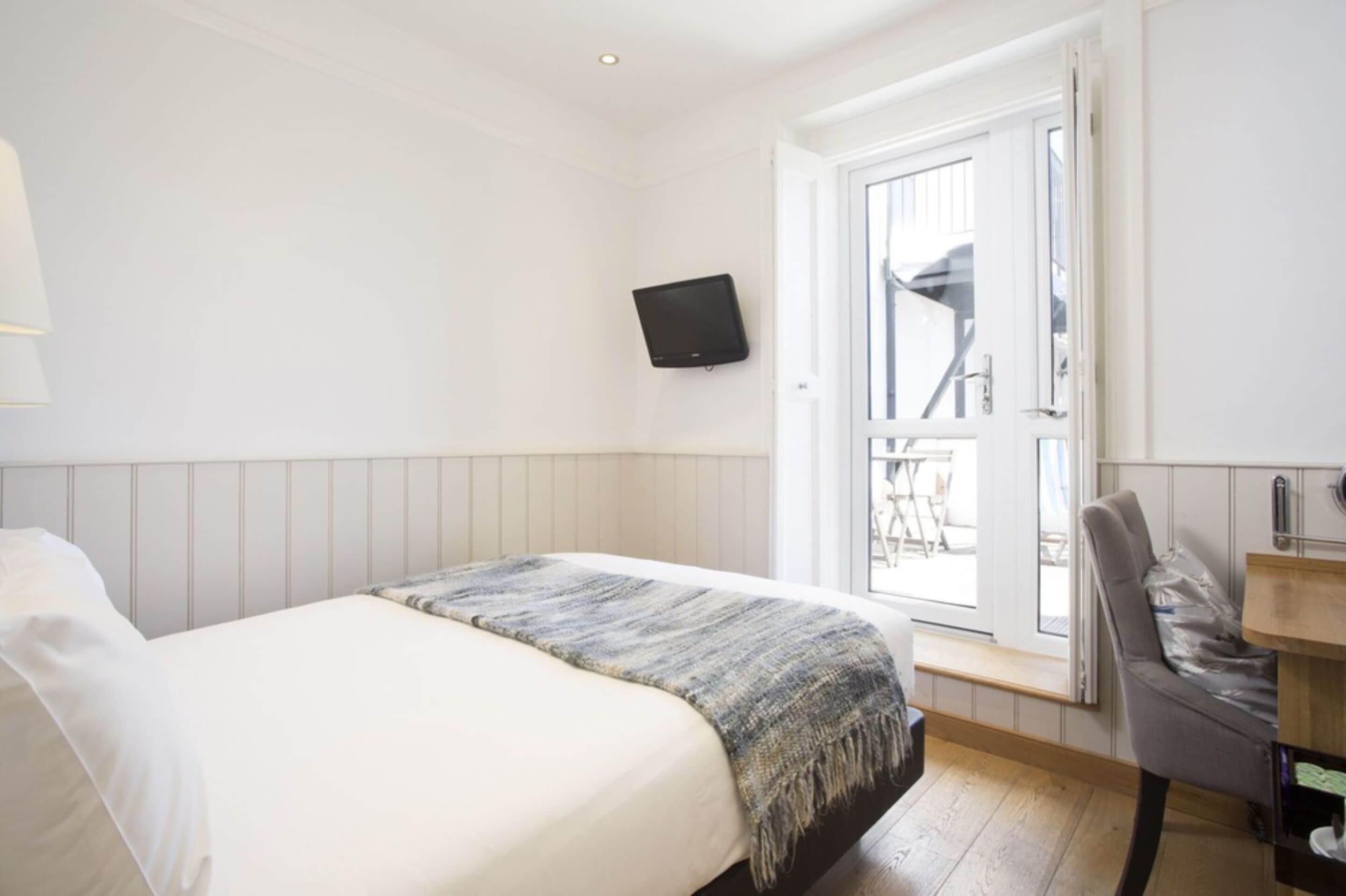A hotel room with a bed, a TV mounted on the wall, a window with a view of the outside, and a chair.