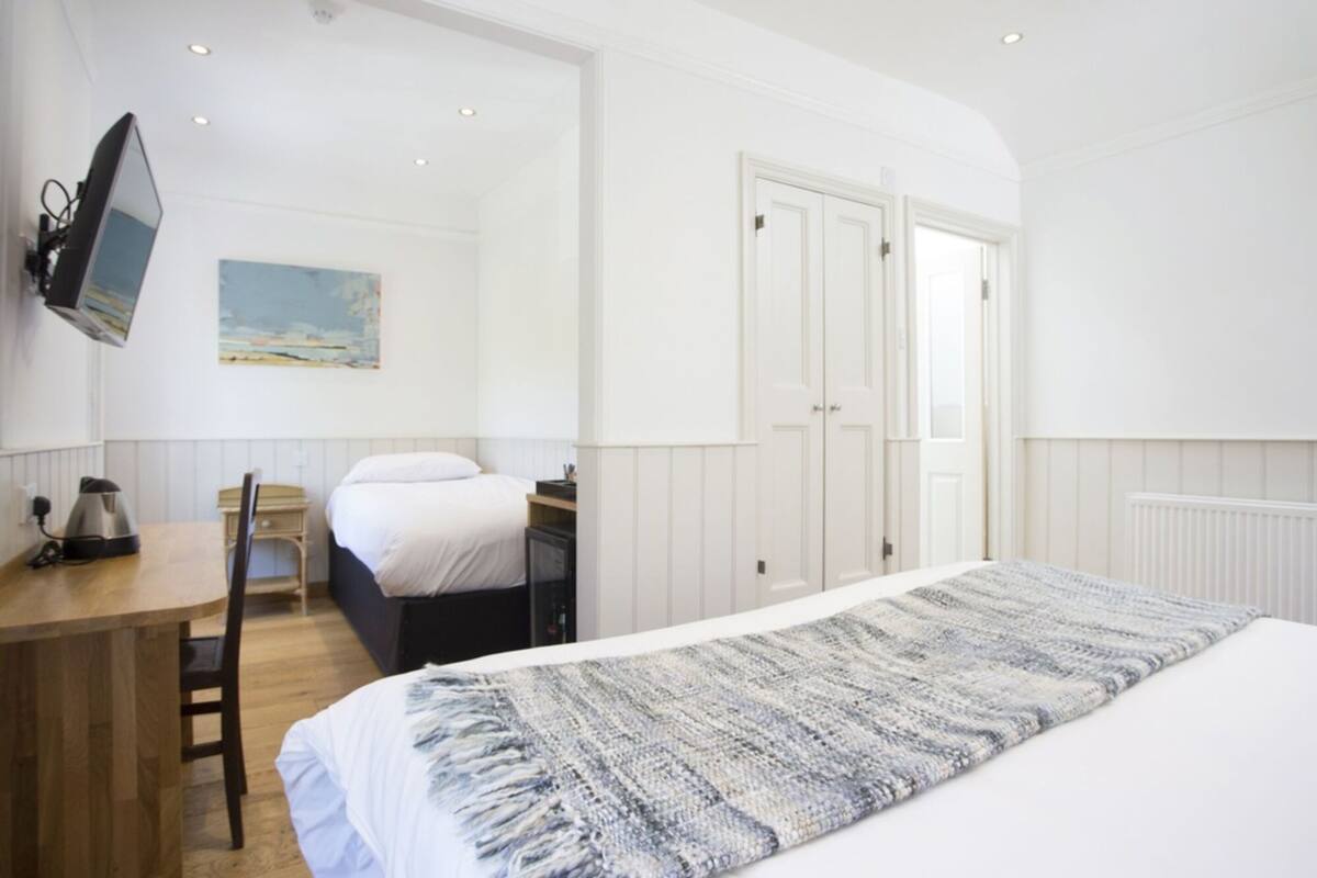 Un dormitorio con una cama, un escritorio, una silla, un televisor montado en la pared y una puerta.