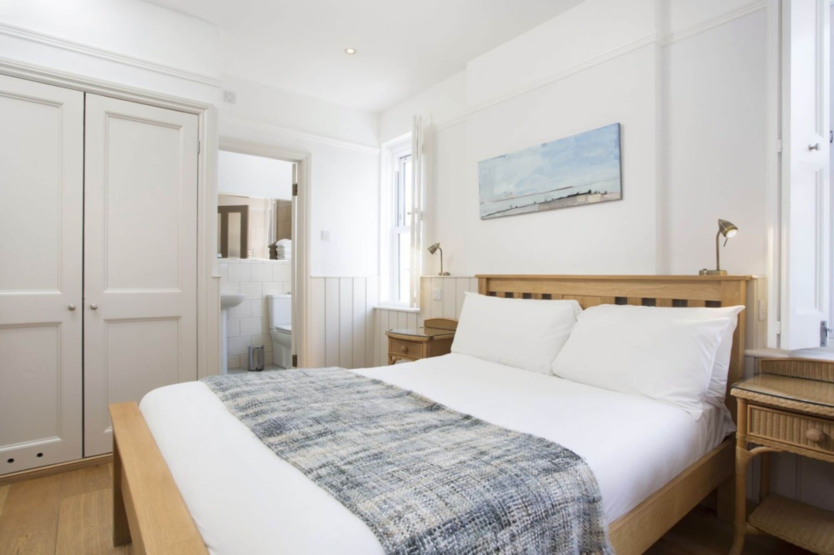 A bedroom with a large bed, a wooden headboard, a bedside table with a lamp, a painting on the wall, and a wardrobe.