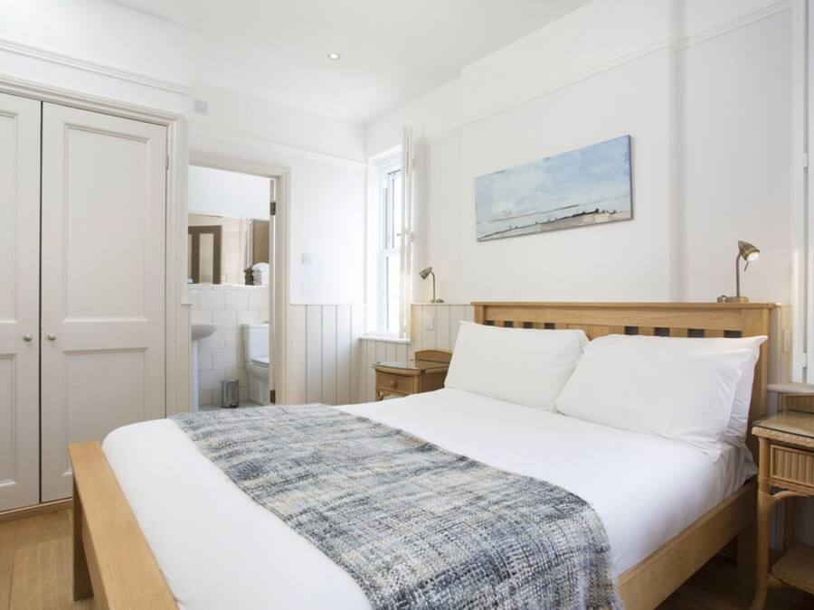 A bedroom with a large bed, a wooden headboard, a bedside table with a lamp, a painting on the wall, and a wardrobe.