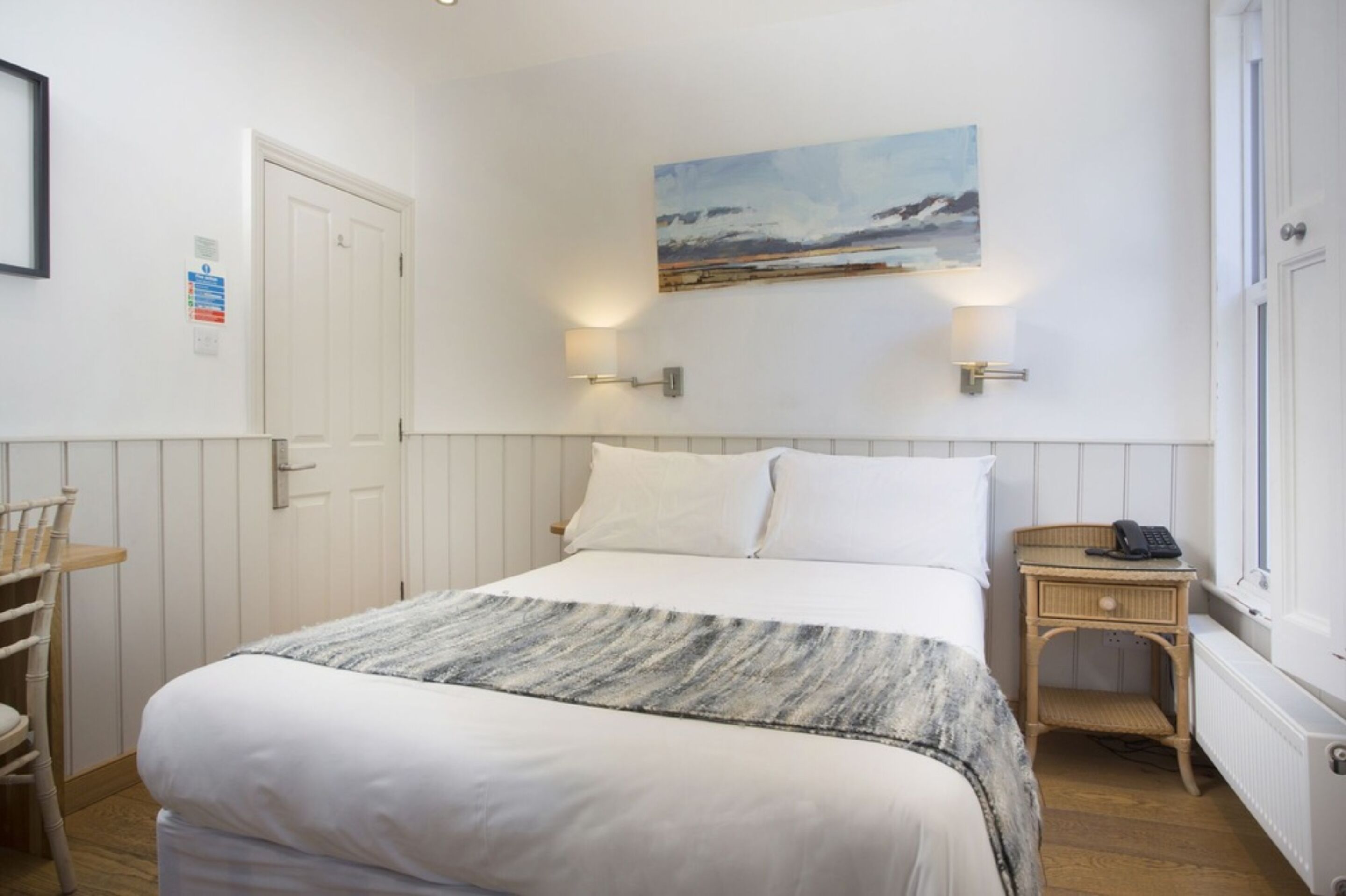 A neatly arranged hotel room with a bed, a bedside table with a lamp, a chair, and a painting on the wall.