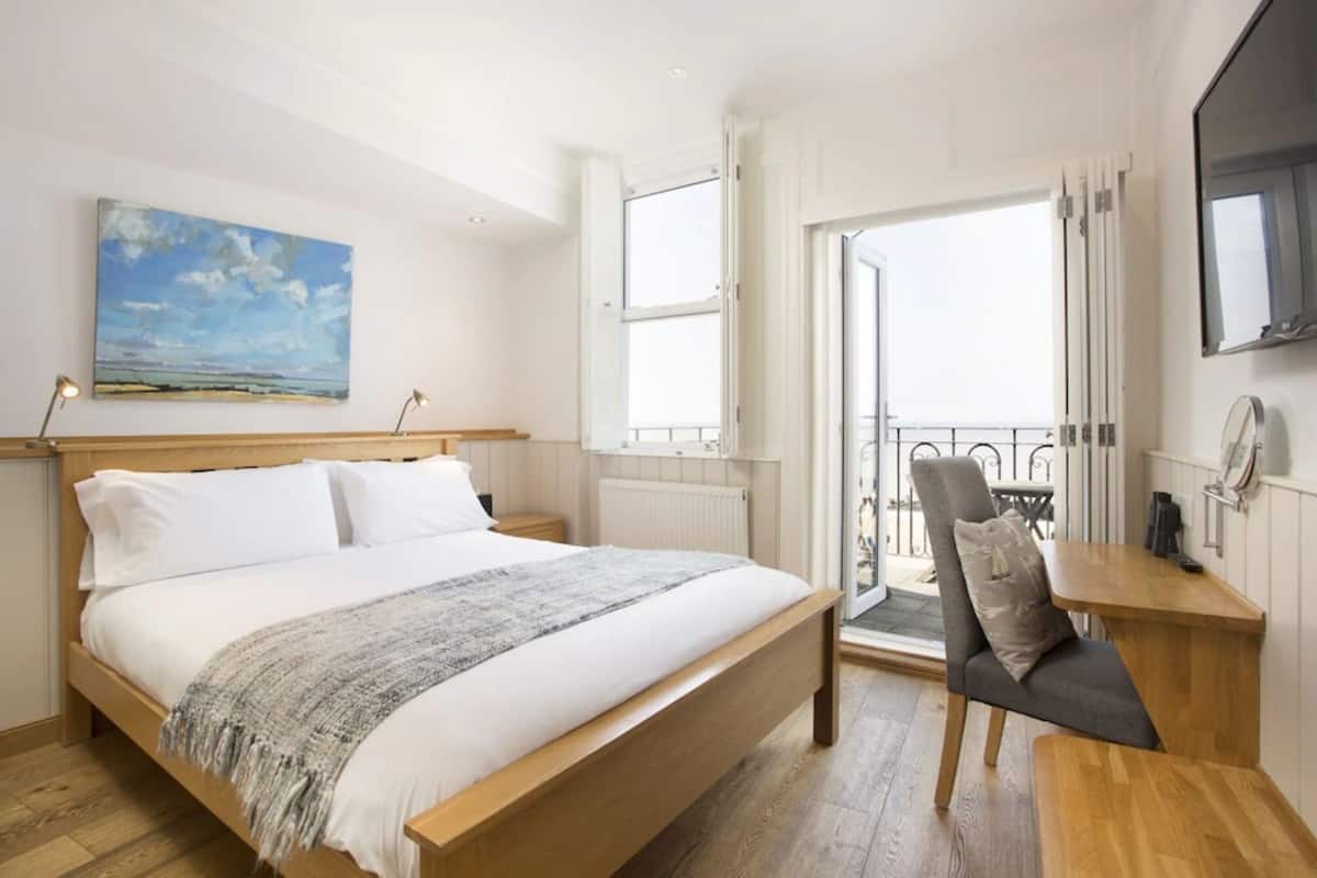 Un dormitorio con cama, una silla, un escritorio, un cuadro y vistas al exterior.