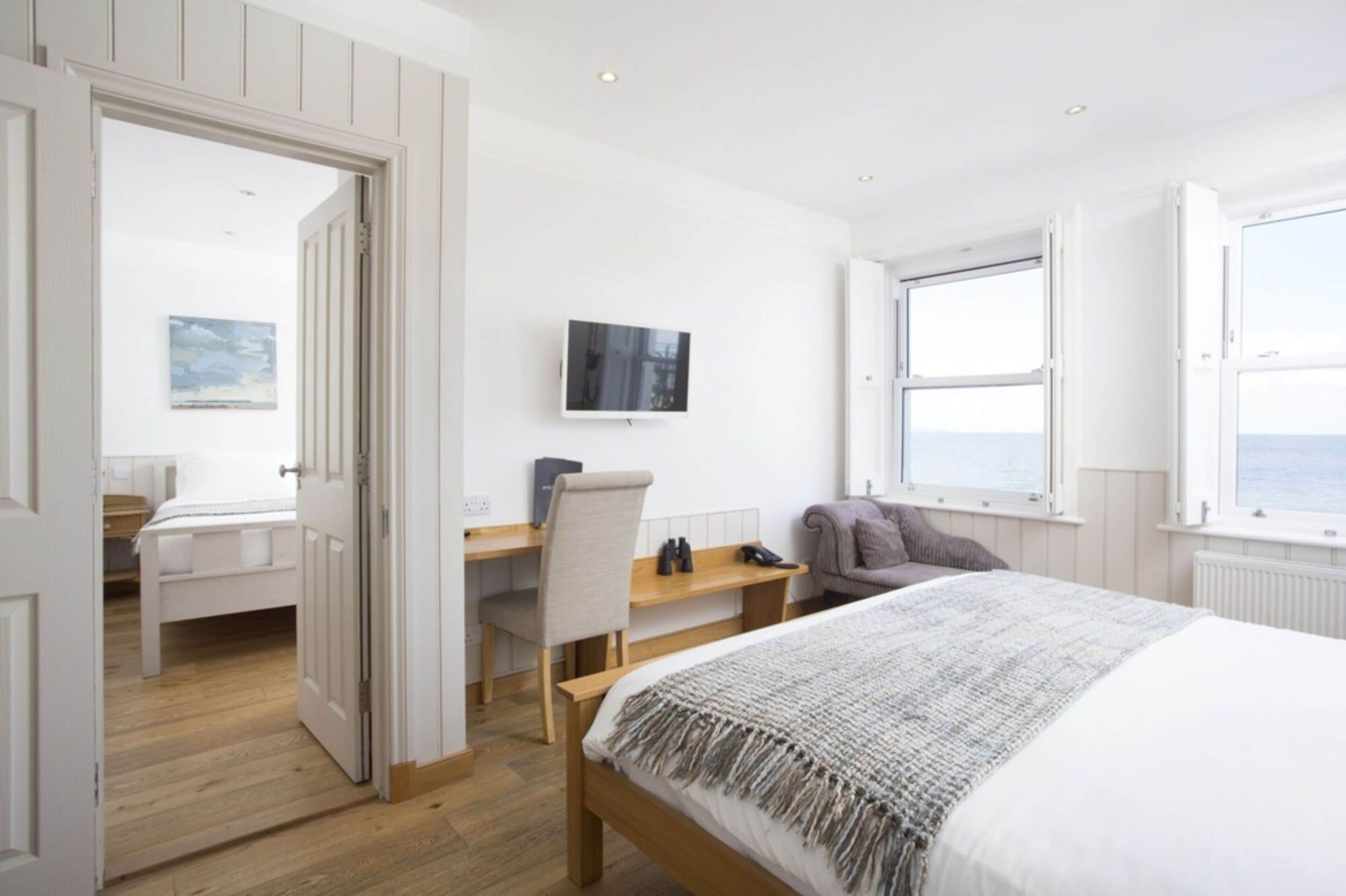 A bedroom with a bed, a desk, a chair, a TV, and a window with a view.