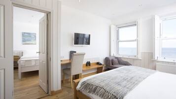 A bedroom with a bed, a desk, a chair, a TV, and a window with a view.