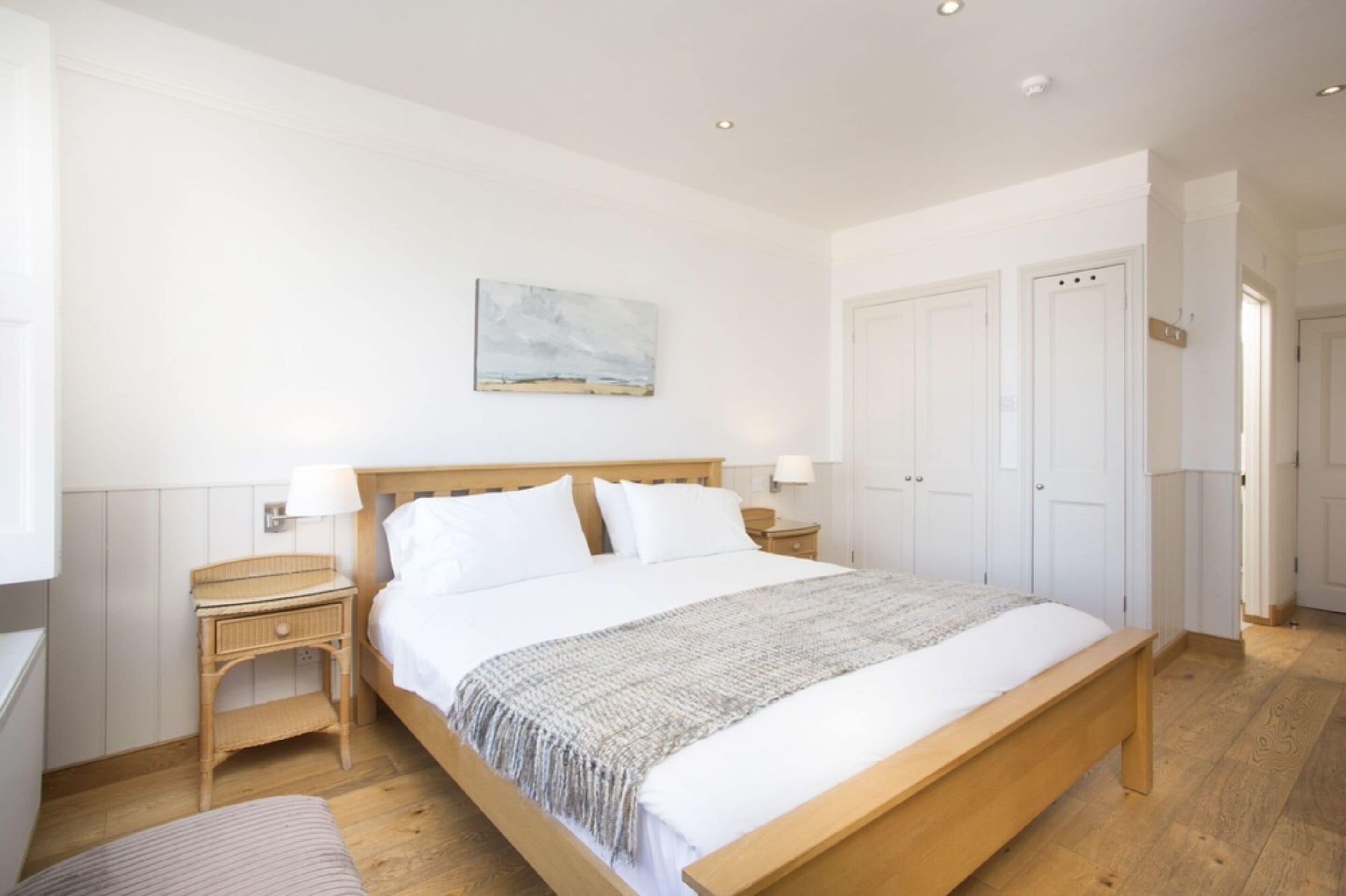 A bedroom with a wooden bed, white walls, a painting, and a door to the right.