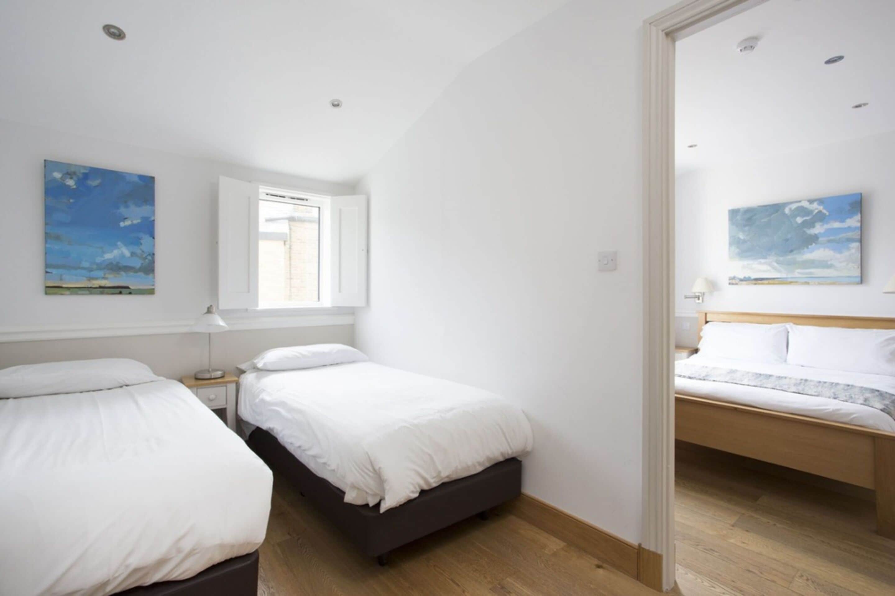 A bedroom with two beds, a window with blinds, and a painting on the wall.