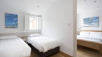 A bedroom with two beds, a window with blinds, and a painting on the wall.