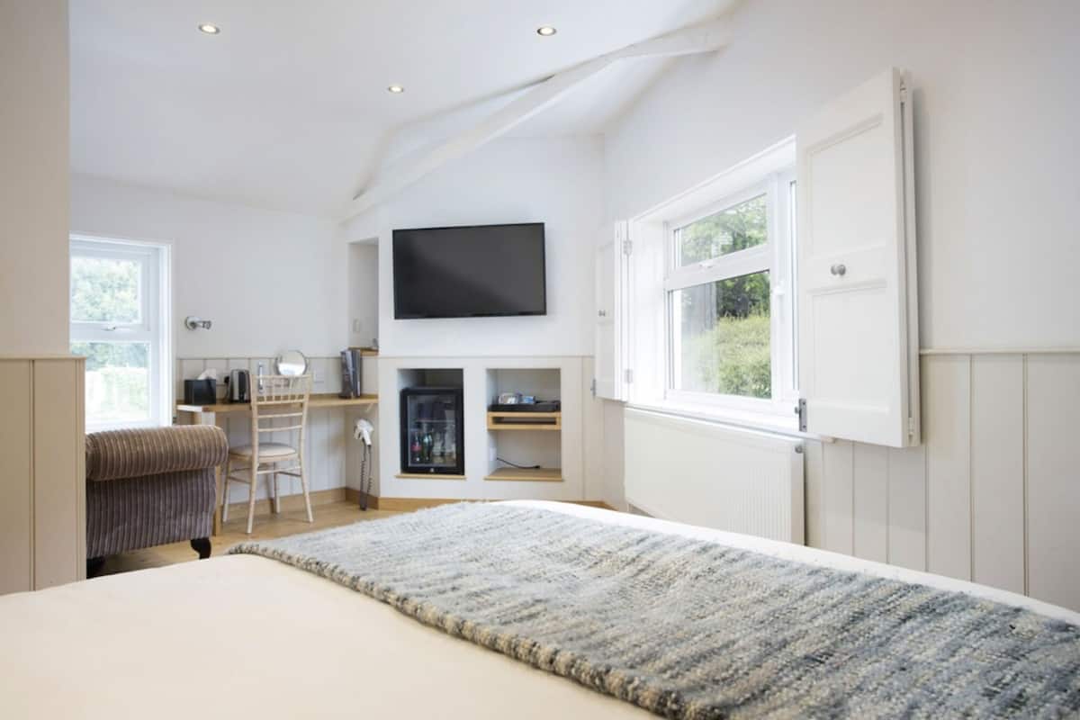 Un dormitorio con cama, televisor montado en la pared, escritorio con silla y ventana.