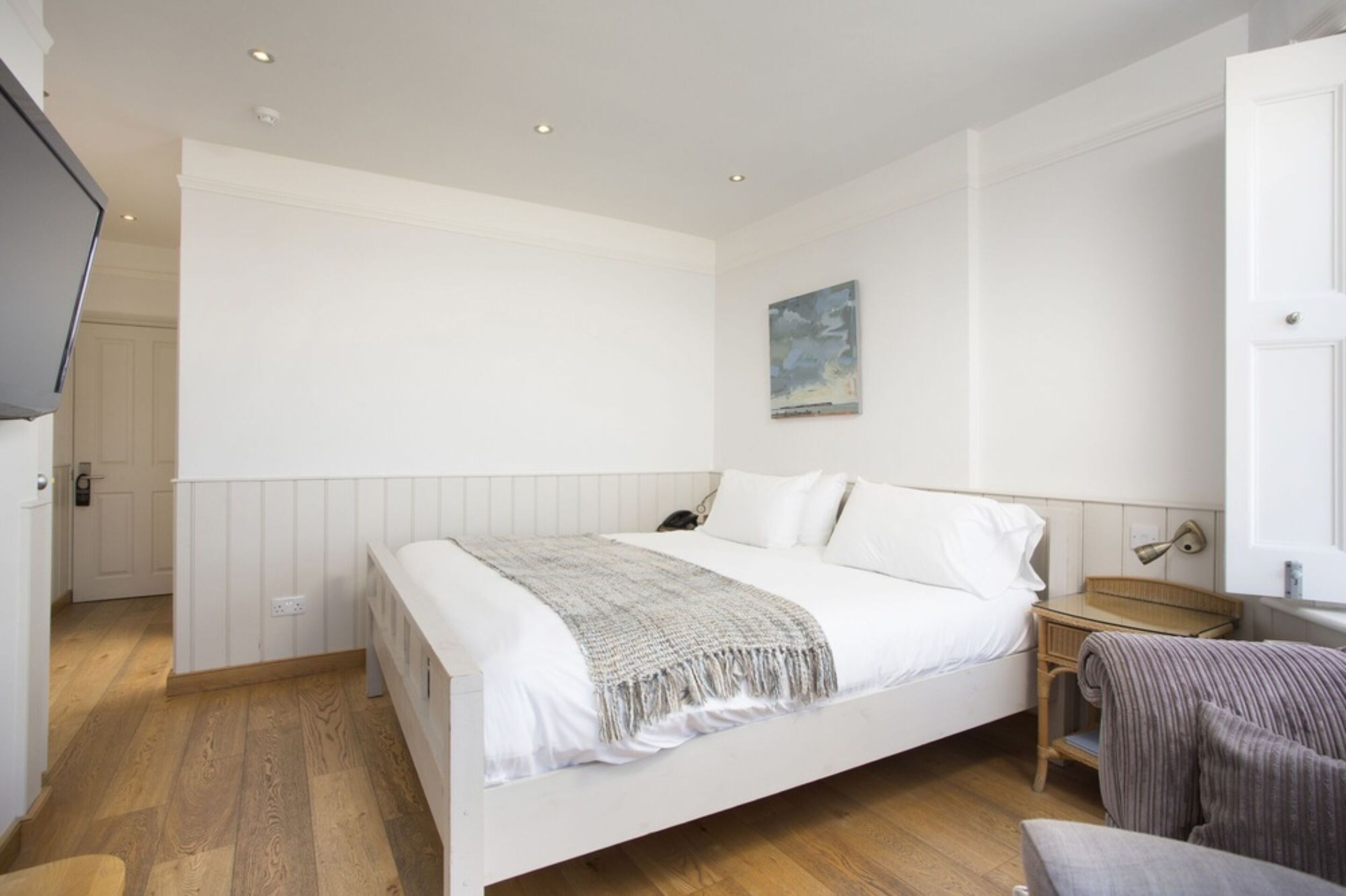 Une chambre à coucher avec un grand lit, une table de chevet, une chaise et un tableau accroché au mur.