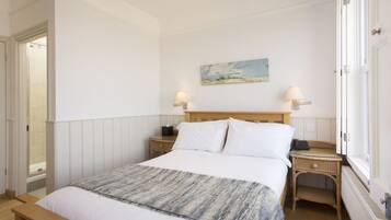 A bedroom with a wooden bed, white bedding, a painting on the wall, two bedside lamps, and a window with a view.