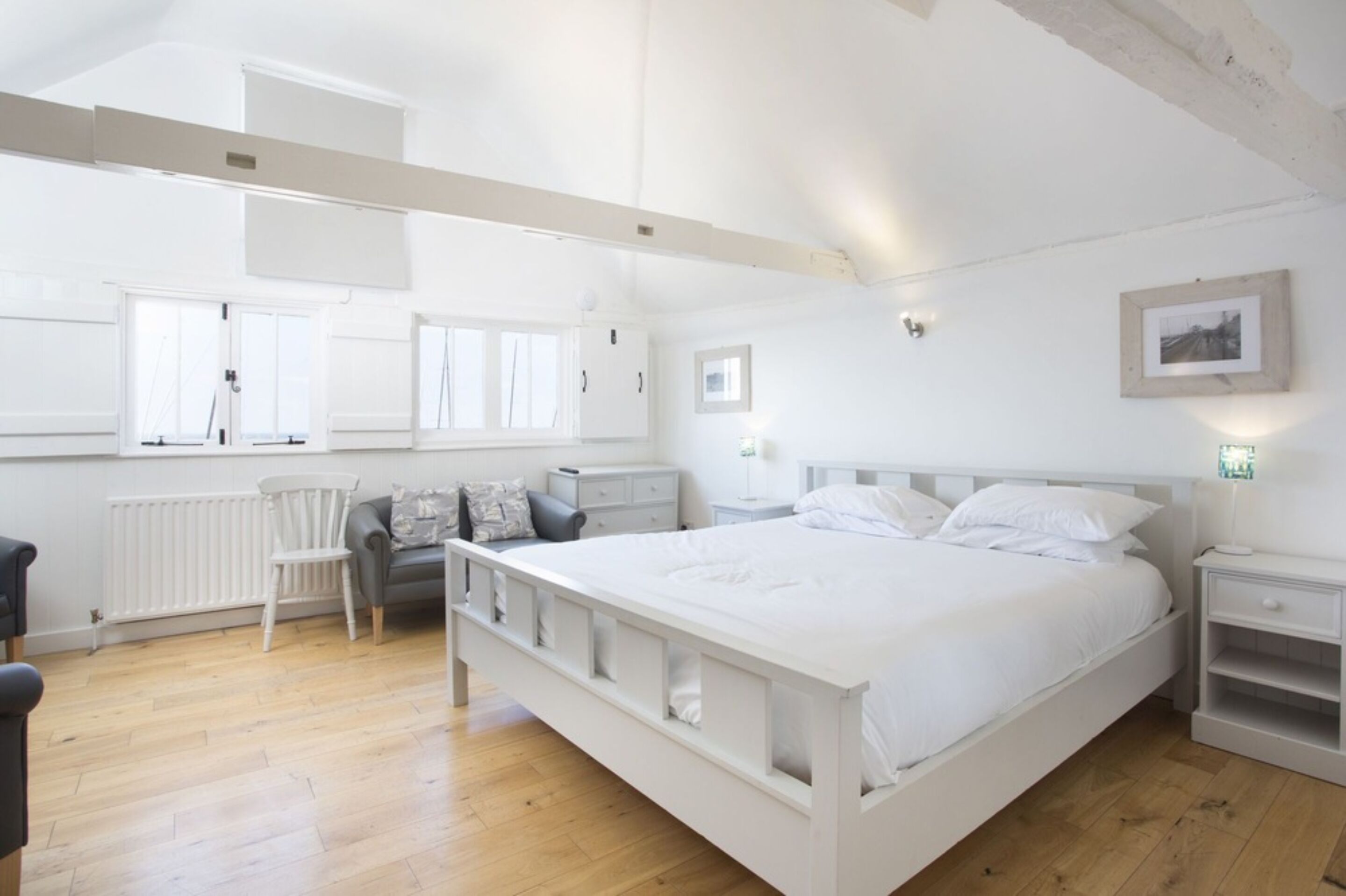 A spacious bedroom with a large bed, a chair, a nightstand, and a window.
