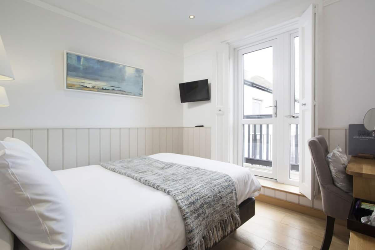 Habitación de hotel con cama, un cuadro, televisor, silla y balcón.