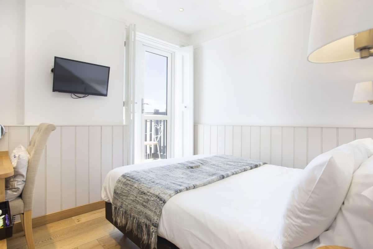 Un dormitorio con cama, televisor en la pared, ventana y puerta que da a un balcón.