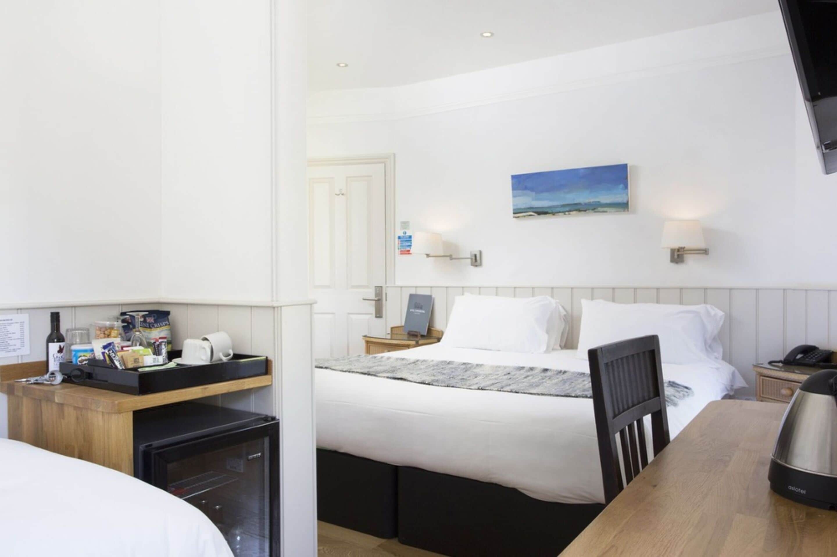 Habitación de hotel con cama, mesita de noche, un refrigerador pequeño, un escritorio de madera y un cuadro en la pared.