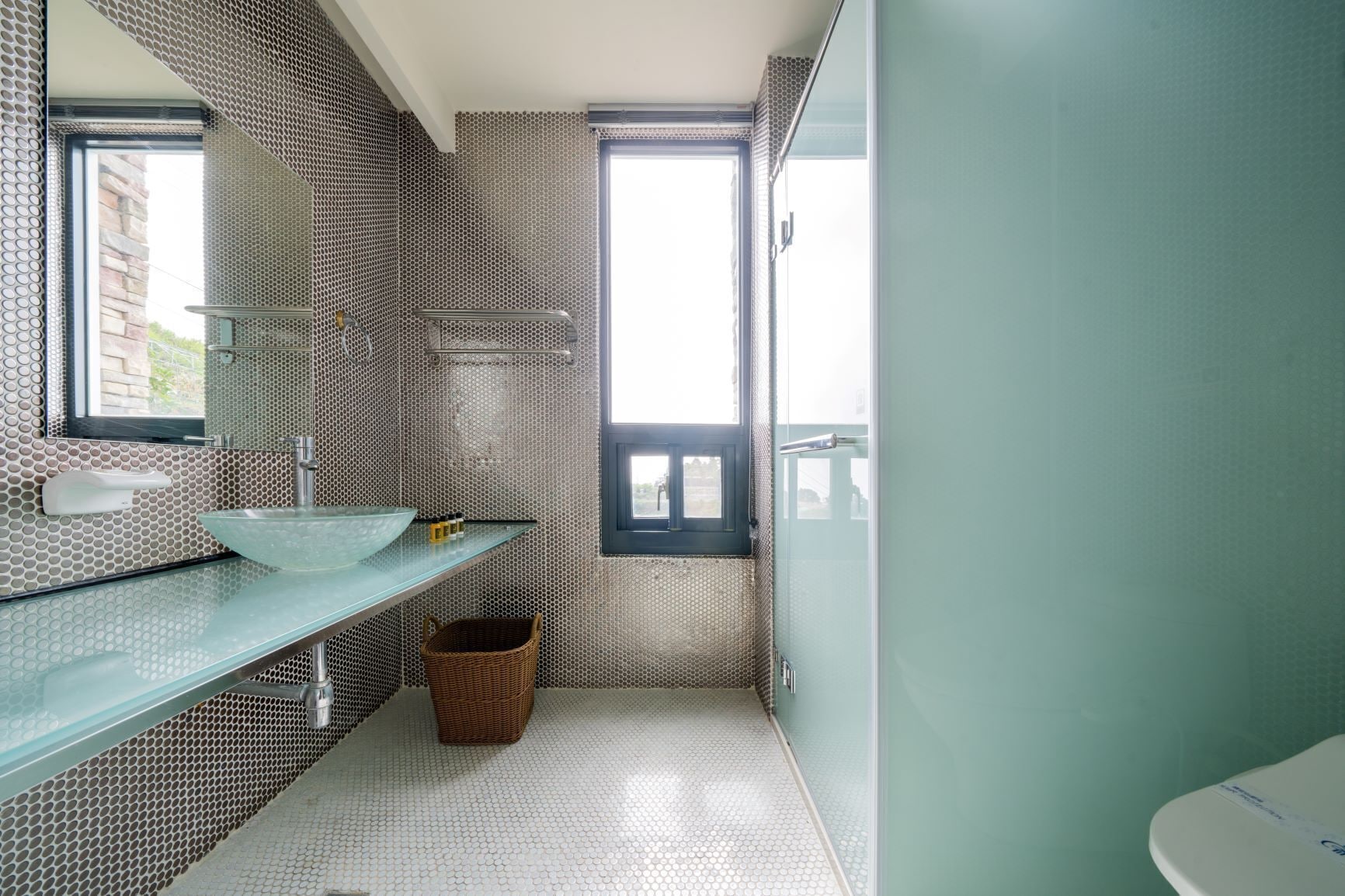 Ein Badezimmer mit einem Glaswaschbecken, einem Korbwäscheschrank und einem Fenster.
