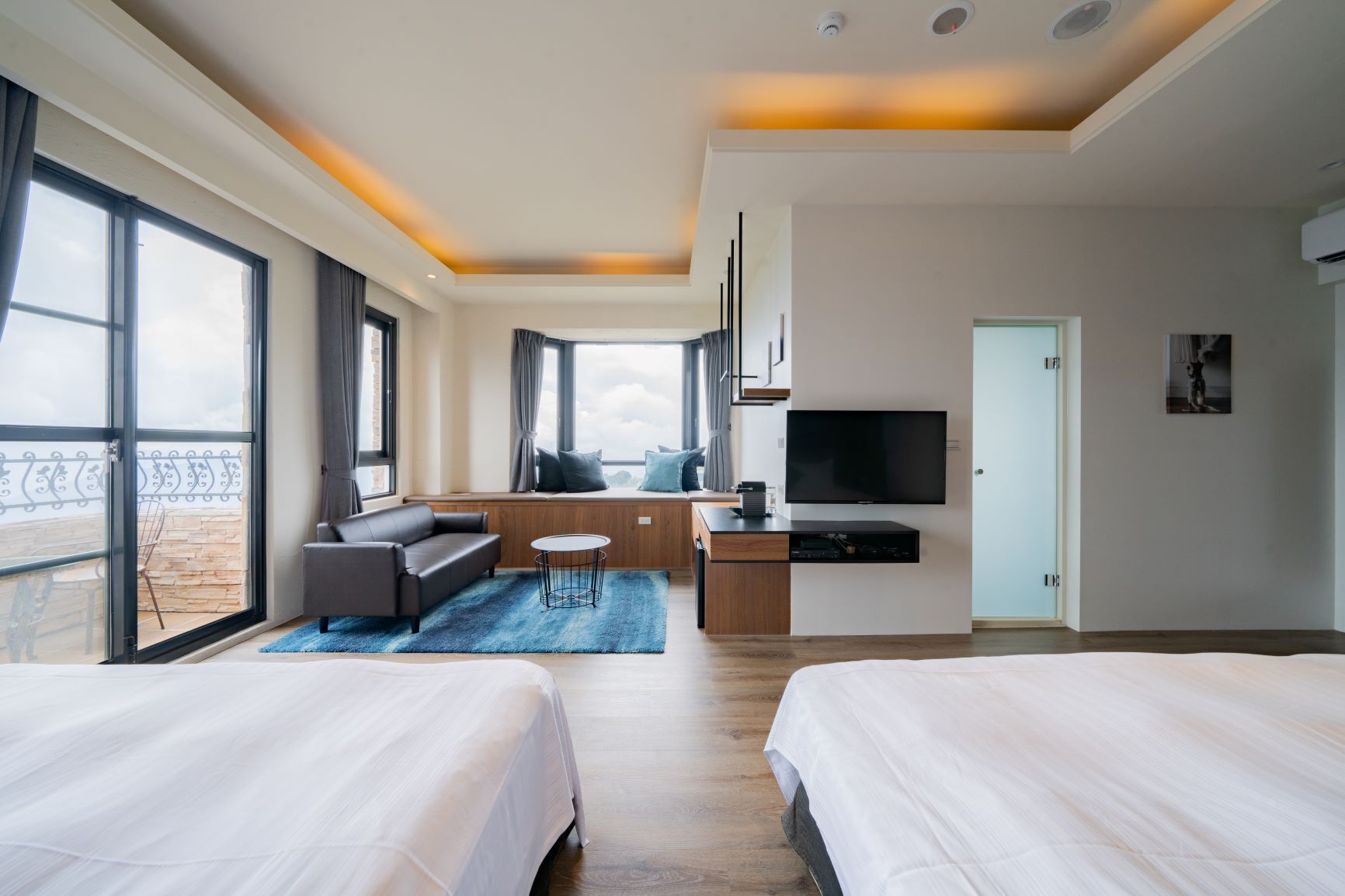 Una habitación de hotel moderna con dos camas, un sofá, una zona de comedor y un televisor.