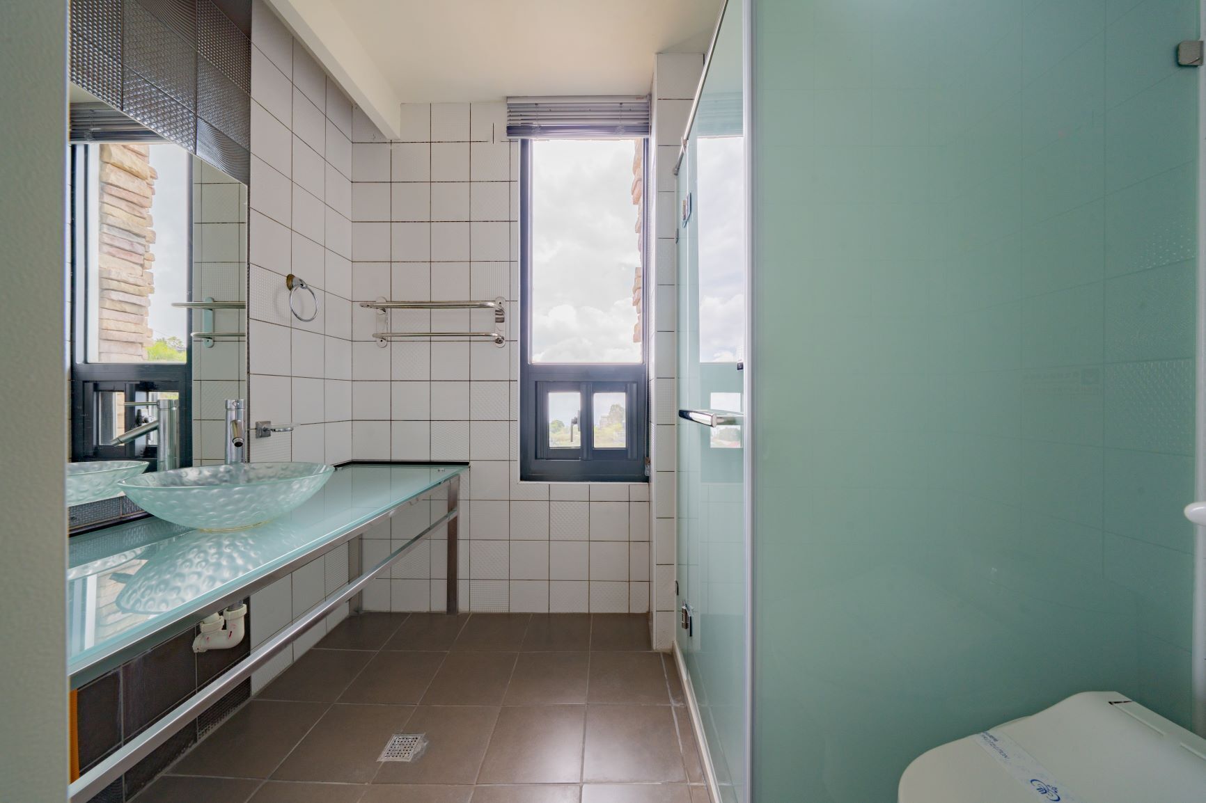 A bathroom with a glass sink, a window, and a toilet.
