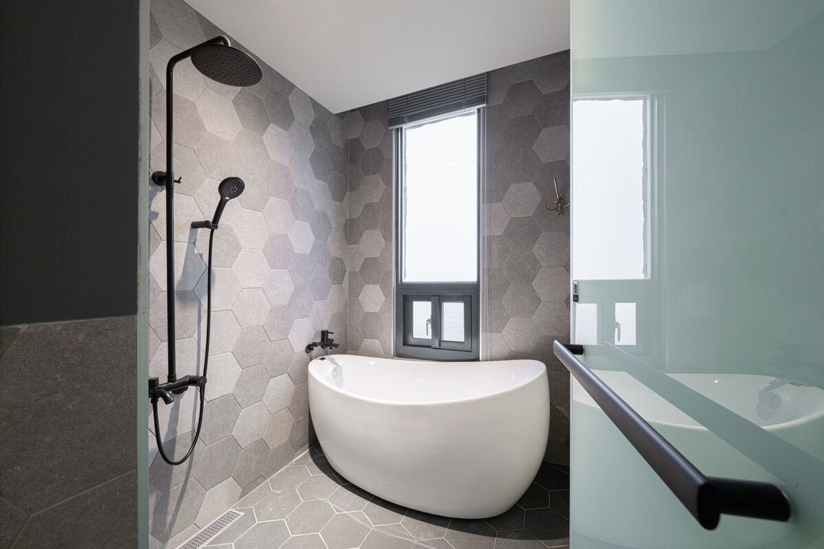 A modern bathroom with a freestanding bathtub, a shower with a handheld showerhead, and a window providing natural light.
