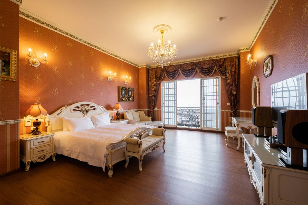 Um quarto espaçoso com uma cama grande, um candelabro e vista para o exterior por uma janela.