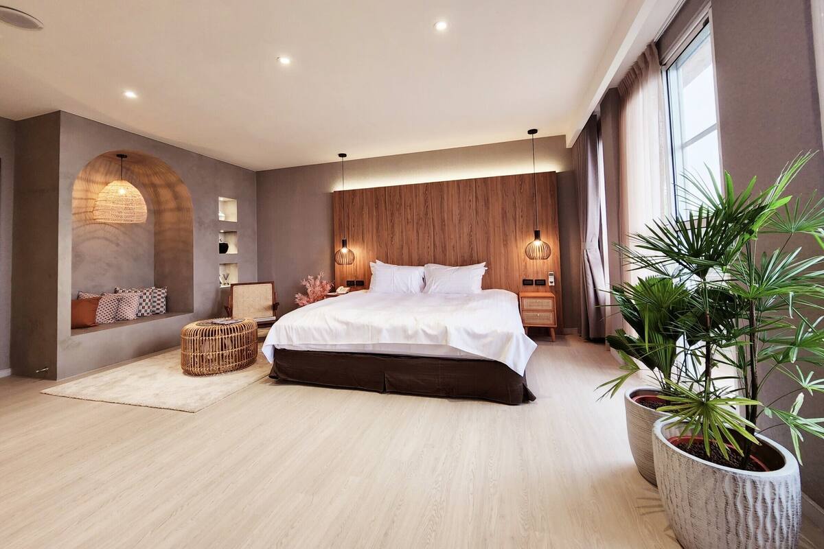 Quarto moderno com cama grande, cabeceira de madeira e um banco embutido com almofadas.