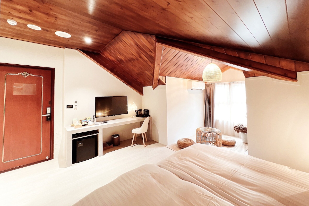 Un dormitorio con techo de madera, una cama, un escritorio con televisor y una pequeña kitchenette.