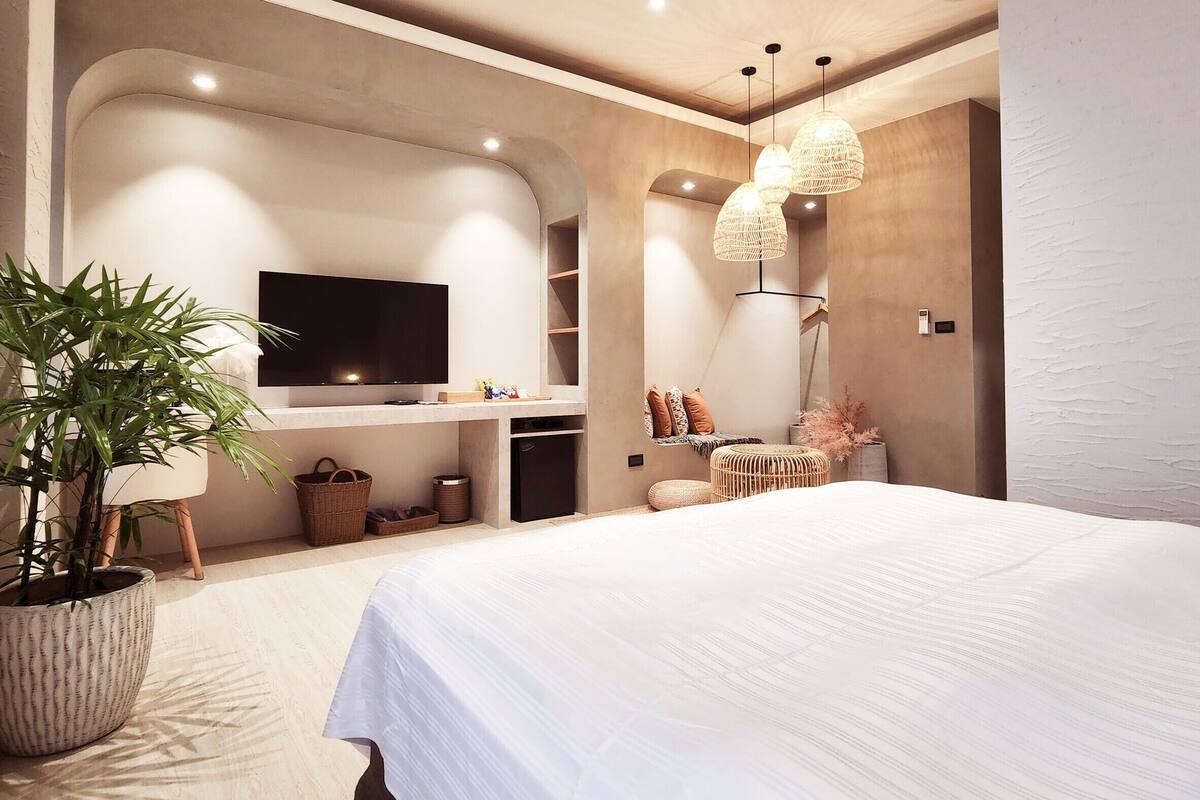 Quarto moderno com uma cama grande, televisão presa na parede, luminária pendente e planta em vaso.