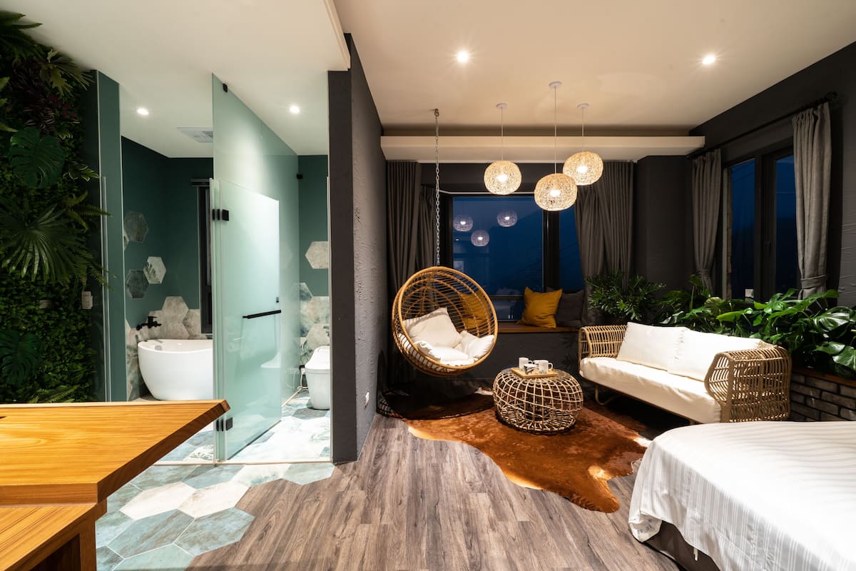 Quarto moderno com cama grande, cadeira suspensa, mesa de madeira e banheiro com banheira.