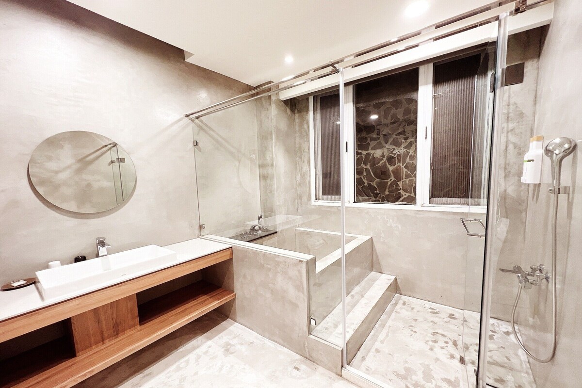 A modern bathroom with a glass-enclosed shower, a round mirror, and a wooden vanity.