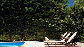 Zona de piscina con sillas de descanso y una pileta, rodeada de follaje denso y una cerca de alambre.