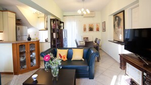 Sala de estar con sofá, mesa de centro y televisor. Se observa una cocina con alacenas y refrigerador.