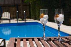 Dos vasos de una bebida transparente con hielo y una rodaja de naranja sobre una terraza de madera junto a una piscina.