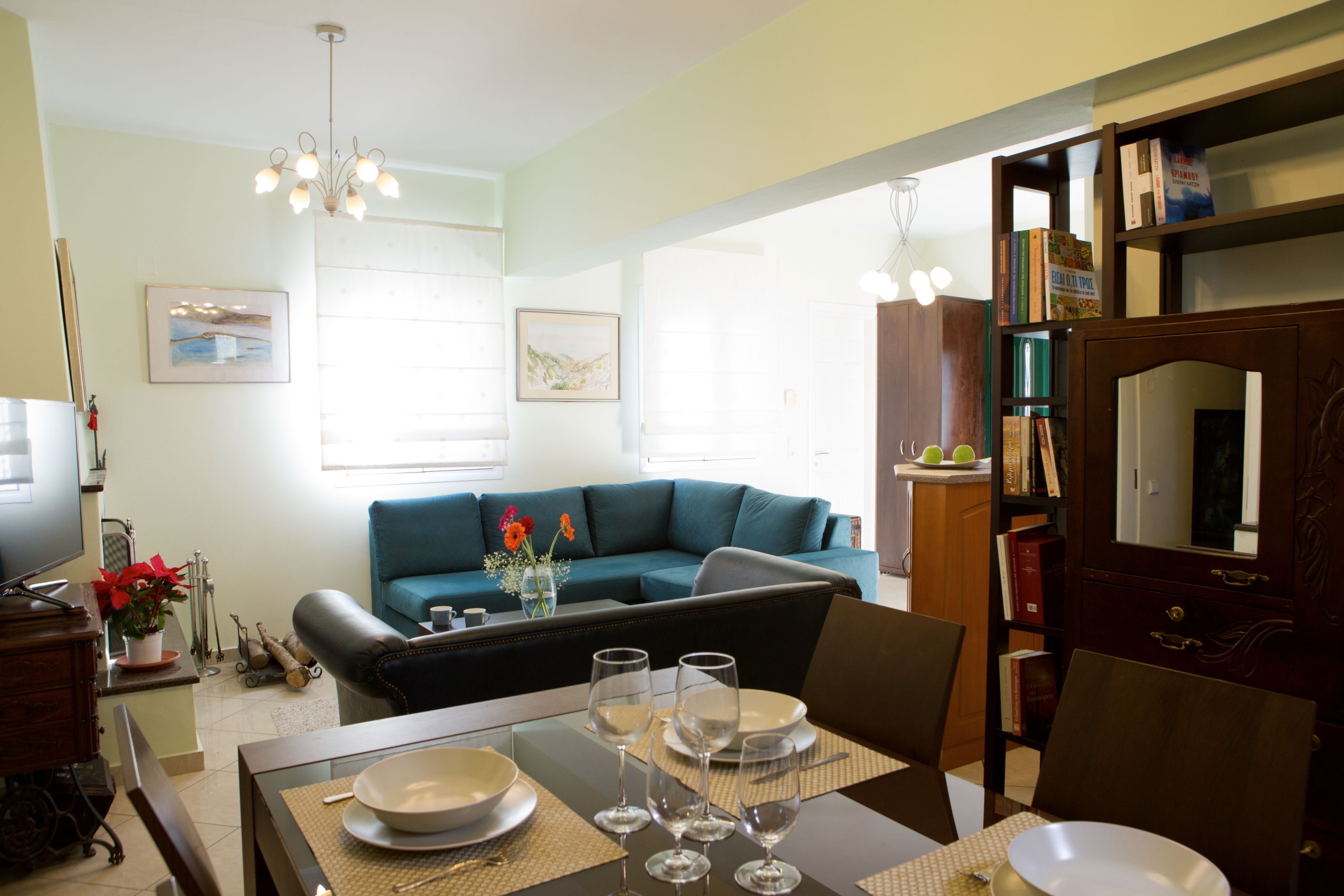 Una sala de estar moderna con un sofá azul verdoso, una mesa de comedor con platos y vasos, y una estantería llena de libros.