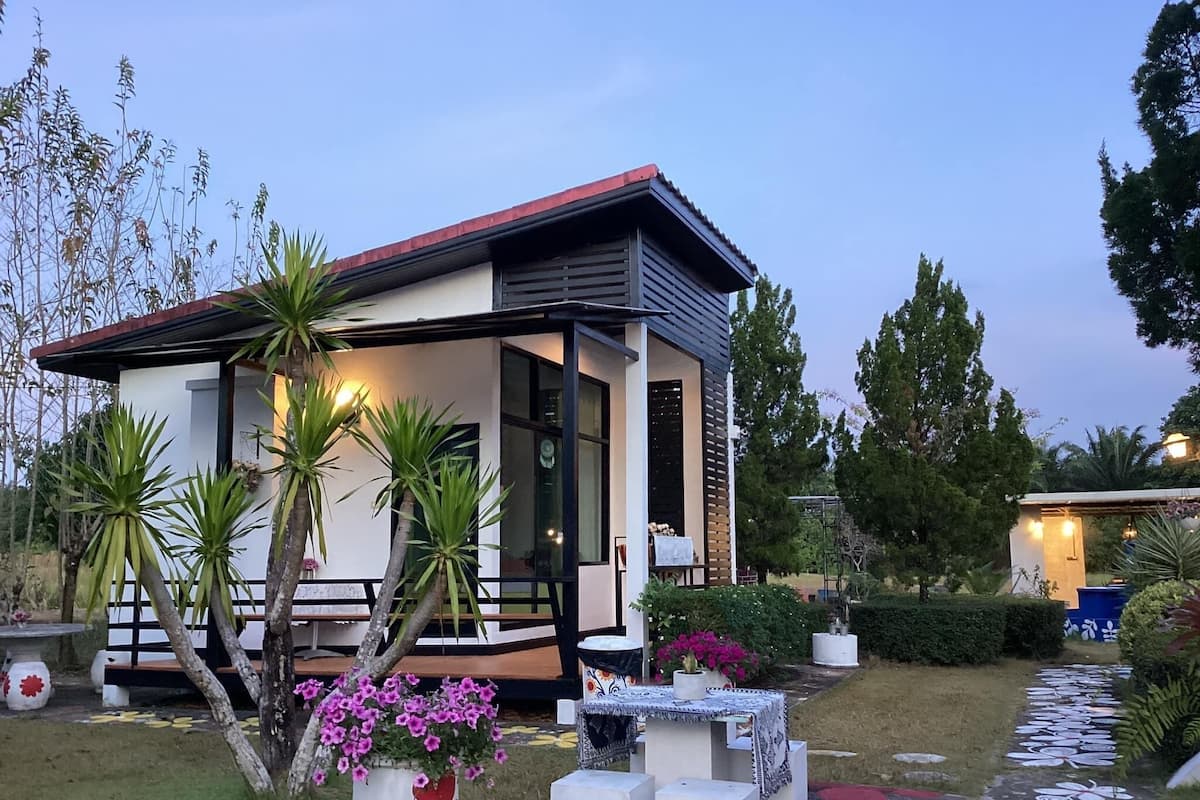 Een modern huis met een overdekte veranda, omgeven door weelderige begroeiing en een decoratief pad.