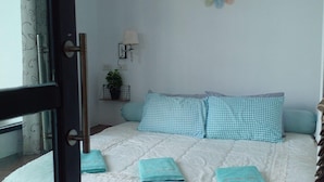 Une chambre à coucher avec un lit, des coussins à carreaux, une horloge murale et une fenêtre avec des rideaux.